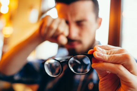 man holding glasses away rubbing eye