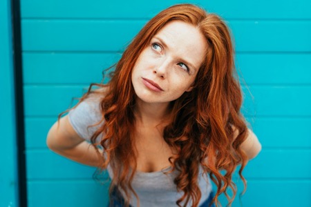 Redheaded woman leaning forwards glancing upwards with curious inquisitive stare