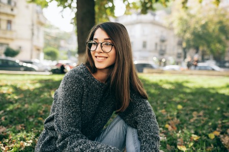 Woman sitting under a tree wearing a gray sweater and glasses