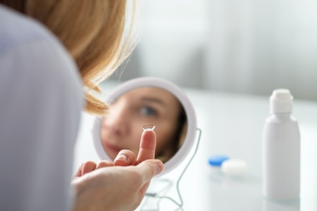 woman looking in mirror with contact lens on finger