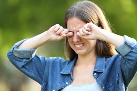 Young woman outside rubbing her eyes caused by dry eye syndrome